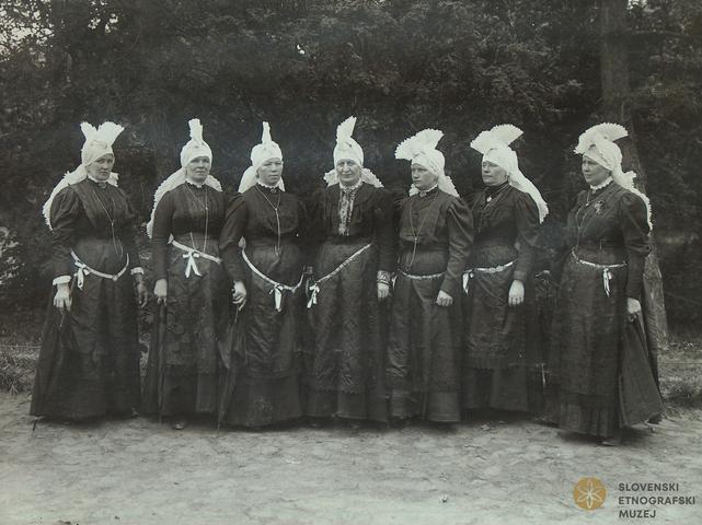 Skupina kostumiranih žena s pečami, vezanimi »na petelina«. Sprevod narodnih noš, Ljubljana, 1908 / Dokumentacija SEM. Skupina kostumiranih žena s pečami, vezanimi »na petelina«. Sprevod narodnih noš, Ljubljana, 1908 / Dokumentacija SEM.
