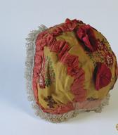 Krstna čepica iz rumenega brokata z rdeče-zelenim cvetličnim vzorcem in belo fino laneno podlogo / Nemški Rovt / iz zbirke SEM / foto: J. Žagar. 