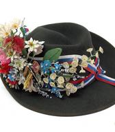 Moški klobuk iz sivega sukna, z mehkim oglavjem in mehkimi krajci; klobuk serijske izdelave, prirejen za nabornika: okoli oglavja je ovit svilen (rips) modro-belo-rdeč trak s pentljo, dodan je še šopek pisanih umetnih rož iz parafina in papirja. Okras za klobuk nabornika je bil izdelan »po starem« leta 1979 / Grabonoš / iz zbirke SEM / foto: J. Žagar. 