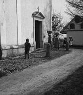 Pražnje oblečene ženske z jerbasi na glavah in otroci s košaricami na poti v cerkev sv. Mavricija.