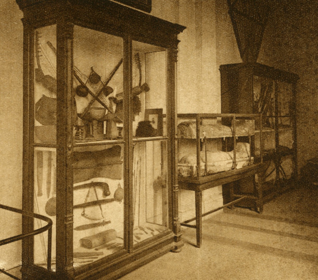 Vitrina z zunajevropskimi predmeti na razstavi v Etnografskem muzeju leta 1929. V vitrini so predmeti iz Sudana, ki sta jih pridobila Lavrin in Knoblehar, glasbila in nekaj orožja pa je iz Gabona pripeljal ladijski kapitan Perčič. Med afriškimi predmeti se je pomotoma znašel tudi leseni kij z okroglim glavičem iz Baragove donacije. Desno od vitrine je razstavljena egipčanska mumija z dvignjenim pokrovom lesene antropomorfne krste. (Ilustrirani Slovenec 5/48, 1. 12. 1929, str. 381, foto: dokumentacija SEM)
