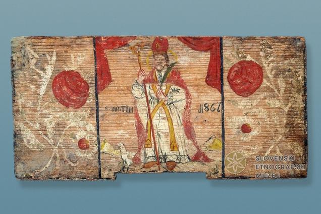 Na fotografiji je panjska končnica iz zbirke SEM, poslikana z motivom sv. Martina v škofovski opravi in z gosjo pri nogah.