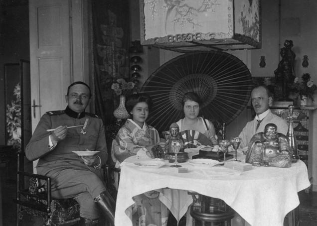 Zakonca Skušek in njuna obiskovalca v dnevni sobi, natrpani s pohištvom in predmeti iz zbirke, dvajseta leta 20. stoletja. Foto: Dokumentacija SEM.