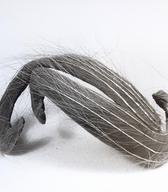 Žensko temensko pokrivalo iz svetlo rjavega žameta, oblikovan v dveh zamaknjenih S linijah; na površini pritrjena vlakna (ali peresa).  Na podlagi napis švicarskega izdelovalca / Ljubljana / iz zbirke SEM / foto: J. Žagar. 