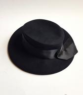 Ženski klobuk iz črne polsti z nizkim ravnim oglavjem, okrašen s širokim svilenim trakom; pražnje pokrivalo šivilje in žene strojevodje, v rabi med svetovnima vojnama in kasneje / Ljubljana, Reka (Hrv.) / iz zbirke SEM / foto: J. Žagar. 