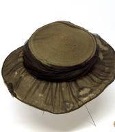 Ženski slamnik iz slamnatih kitic, z ravnim vrhom na oglavju in z mehkimi asimetričnimi krajci; pokrivalo je v celoti prekrito z mehkim sivim tilom. Pred 1. svetovno vojno ga je nosila modistka / Ljubljana / iz zbirke SEM / foto: J. Žagar. 