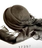 Ženski klobuk iz črne polsti, z okroglim oglavjem in izrazito navzgor upognjenimi krajci in asimetrično pentljo. Za žalno rabo je bil klobuk dopolnjen s črno tančico, ki je mehko zavezana okoli oglavja. V 30. letih 20. stoletja ga je nosila žena krojača / Ribnica / iz zbirke SEM / foto: J. Žagar. 